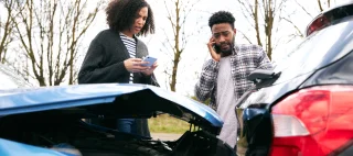 Man and woman on their phones after having gotten into a wreck – cheap liability insurance.