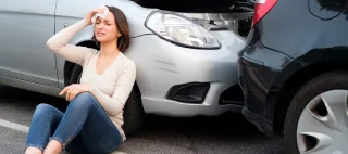 Woman sitting on ground holding a cloth to her head looking distressed after a wreck – cheap liability insurance.
