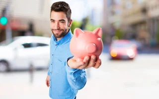 Young man holding a piggy bank with a car in the background – cheap car insurance.