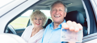 Portrait of a happy senior man showing his available driving license while sitting in the car next to his cheerful wife