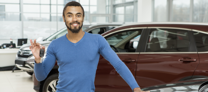 Attractive cheerful young African man smiling showing car keys to his new auto – cheapest car insurance.