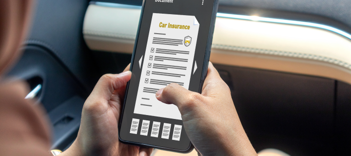 A woman in a car using a mobile phone to read car insurance policy– cheapest car insurance.
